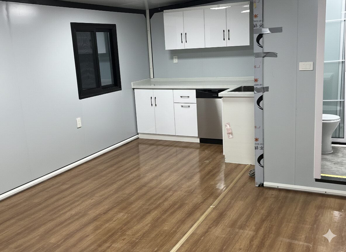 Comanche container tiny home living area with wood-look flooring and a white kitchenette